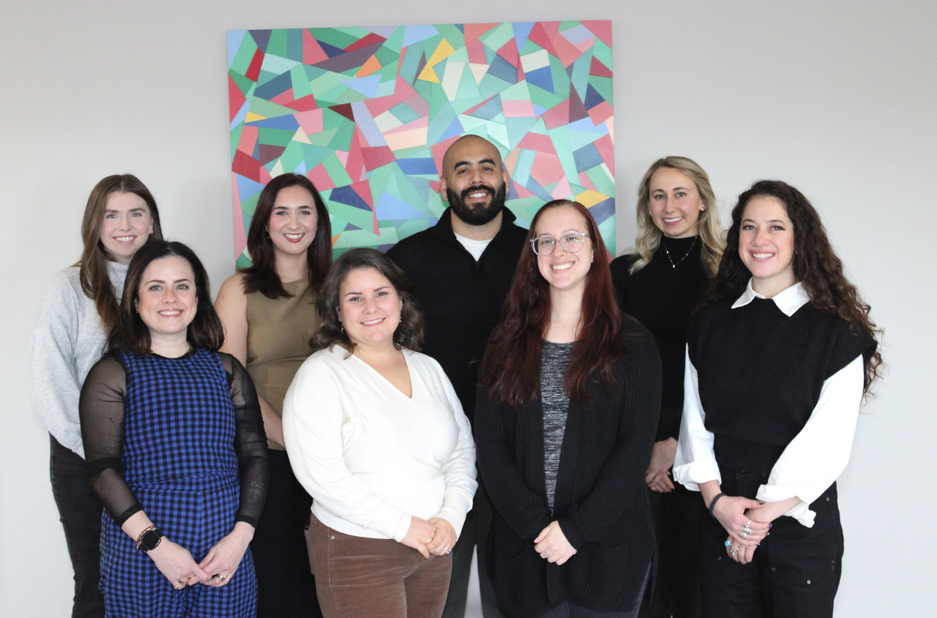 The Better You Institute therapy team: one male and seven female therapists, all smiling and standing with various outfits and hair color. In front of a colorful piece of art.