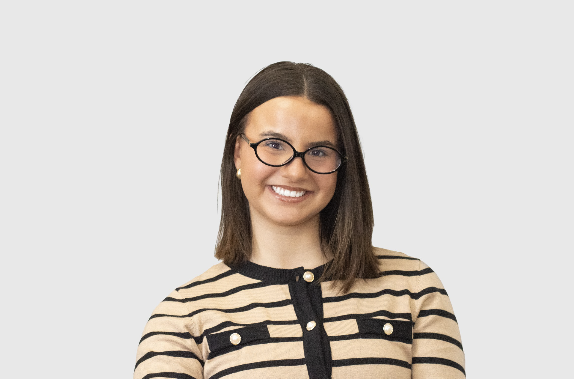 Alyssa Sherwood, MFT intern with dark brown shoulder-length straight hair (one side tucked behind her ear), black rimmed glasses, and tan and black striped buttoned sweater