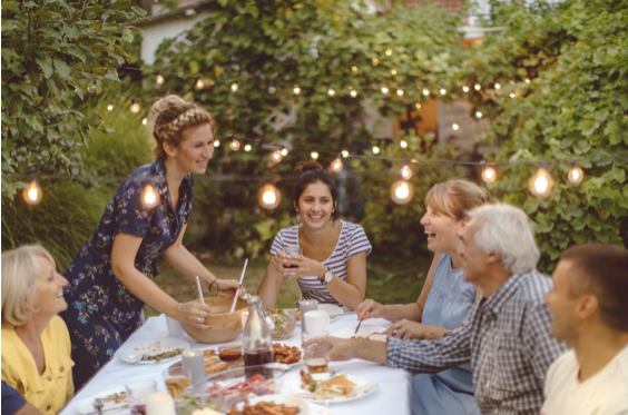 Adult family laughing having dinner in a garden with twinkle lights.
