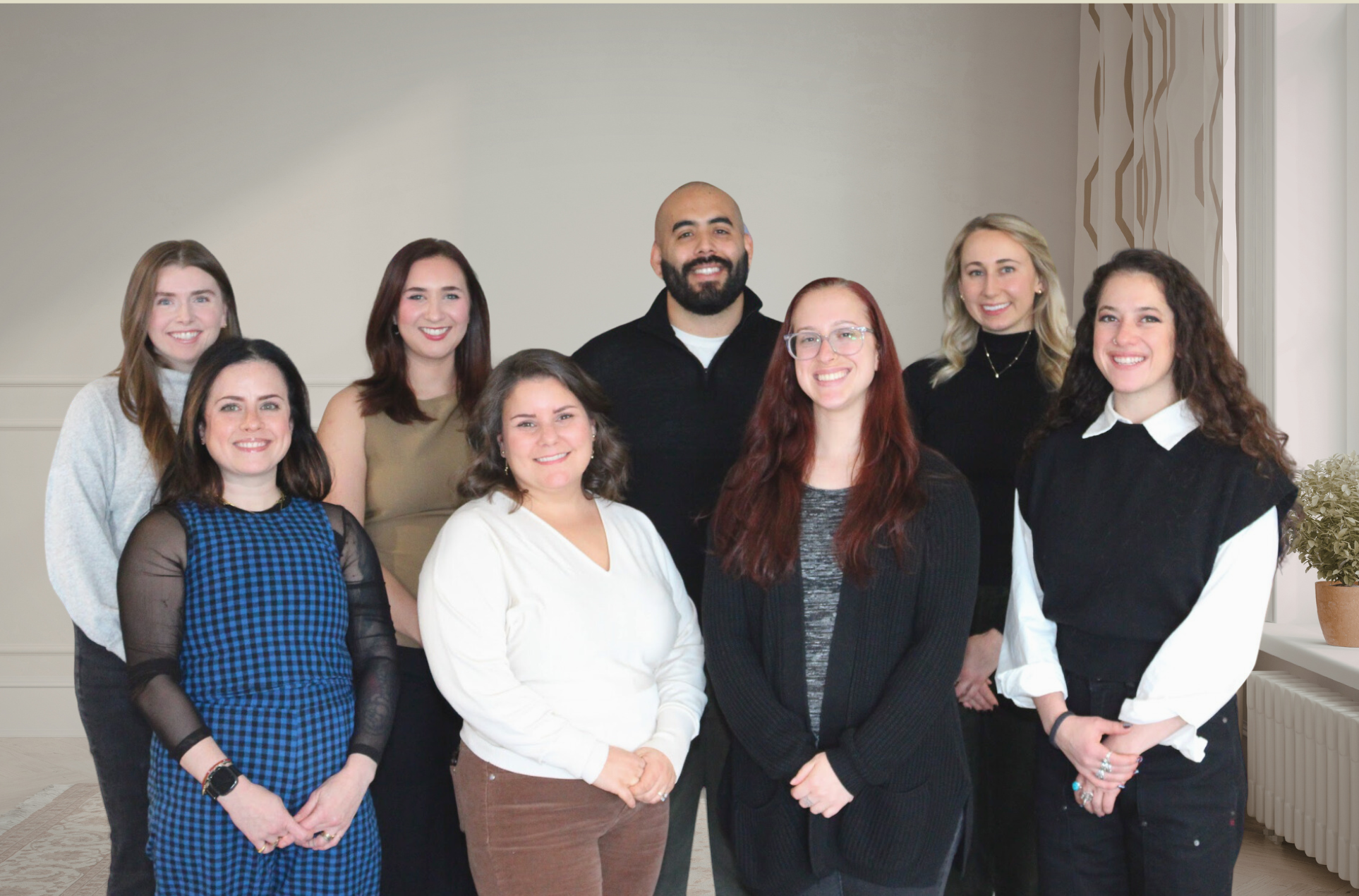 The Better You Institute therapy team: one male and seven female therapists, all smiling and standing with various outfits and hair color. On the side of a tall window with a house plant.