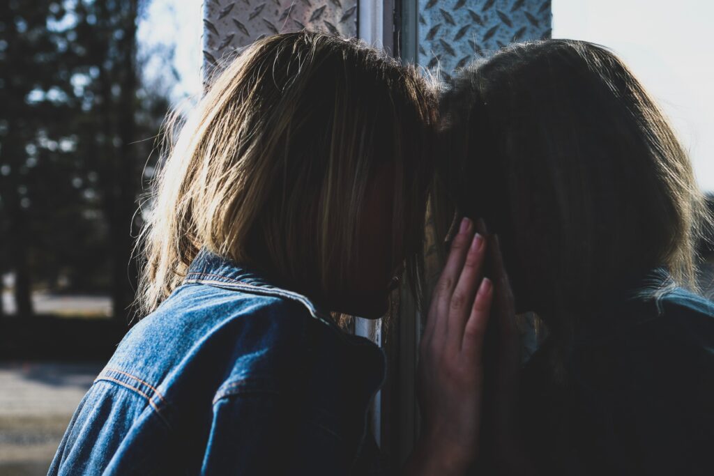 A person leaning their head against a reflective surface, with their hand touching the glass, symbolizing stress, introspection, or emotional struggle