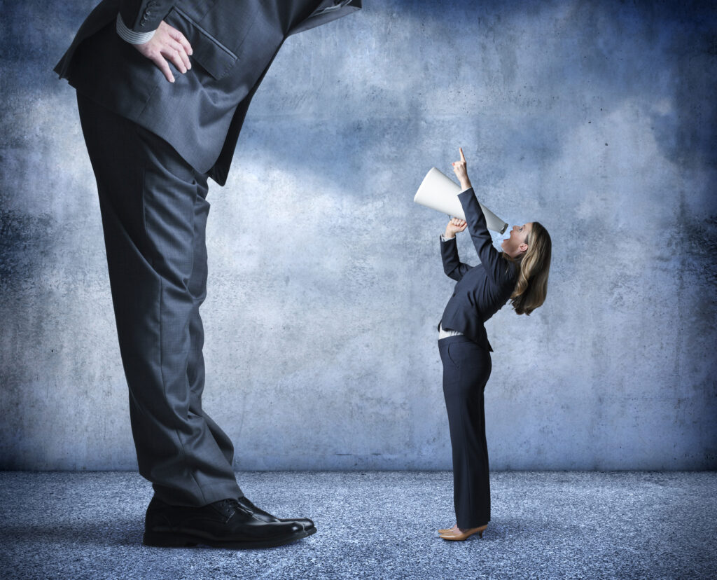 A businesswoman shouts through a megaphone and points up towards a much larger businessman who is standing over her