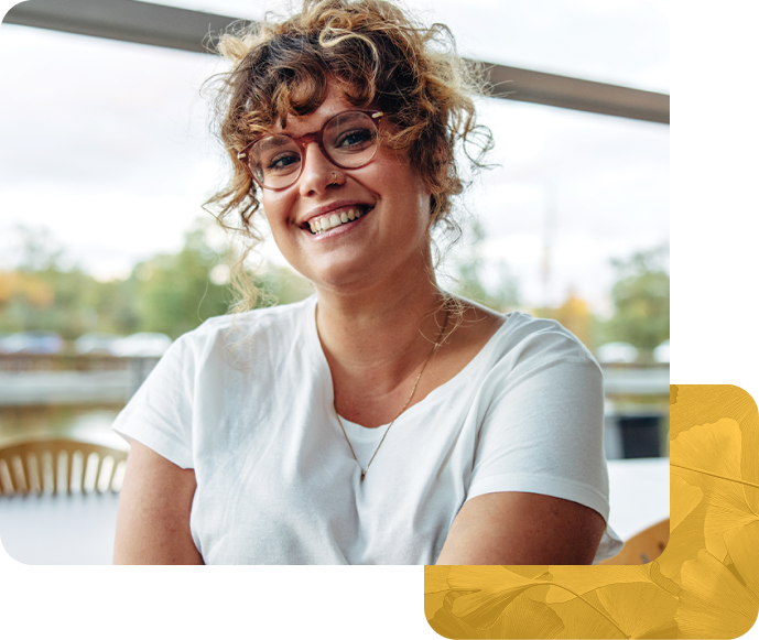 Smiling woman with curly hair and glasses sitting indoors in white shirt