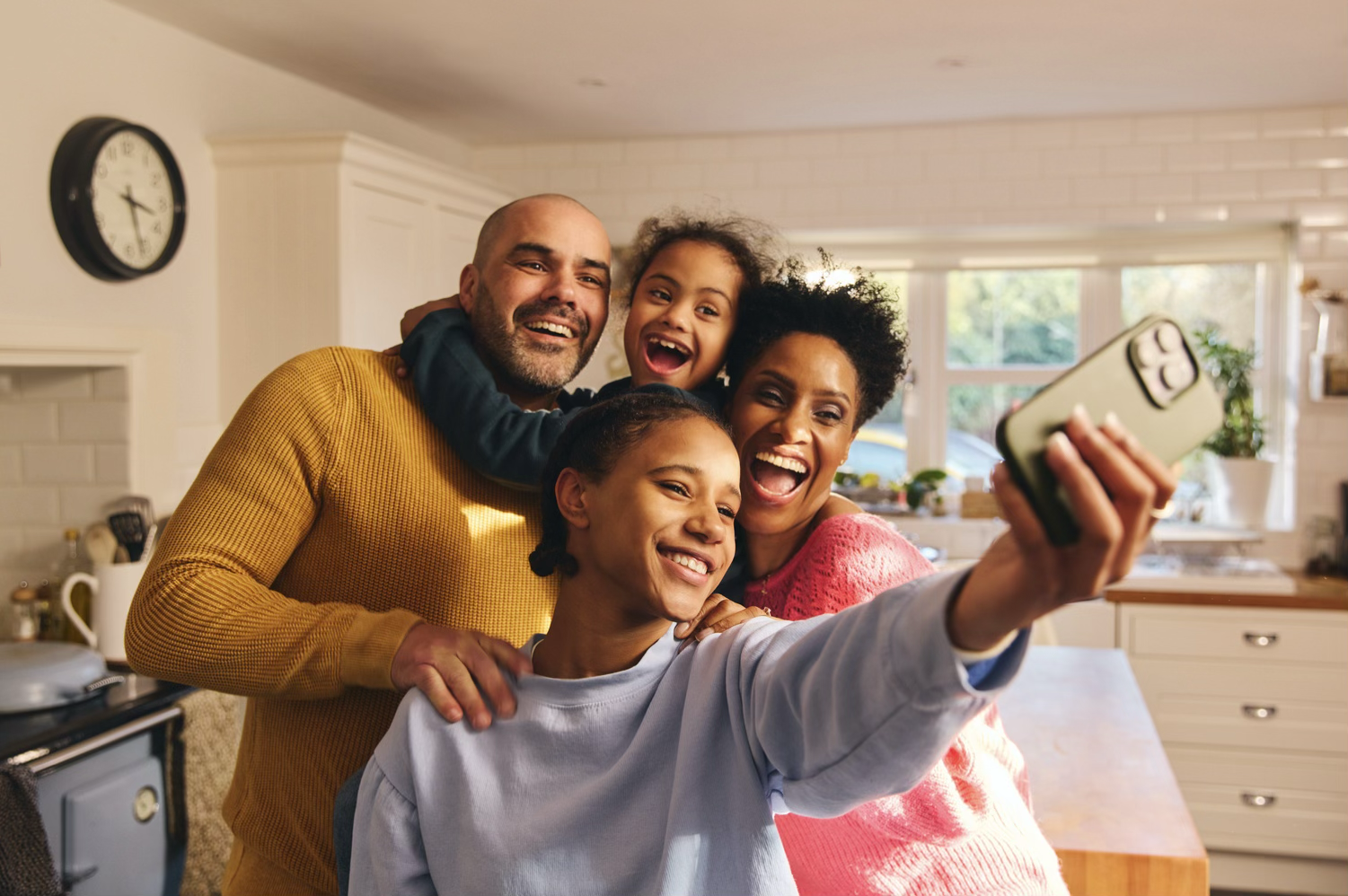 Family smiling together while taking a selfie in their kitchen.