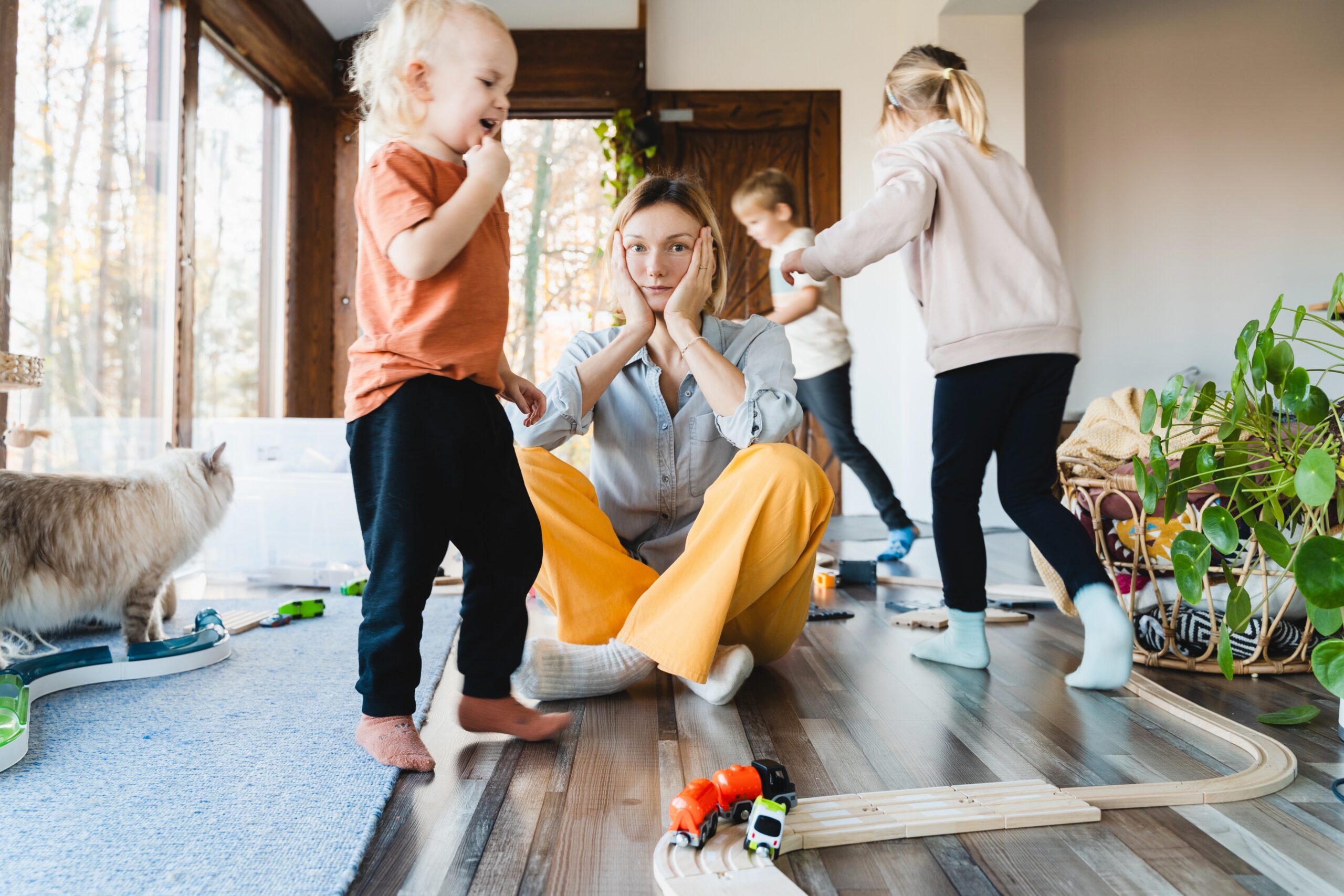 Stressed mother sitting on floor surrounded by active children and household chaos