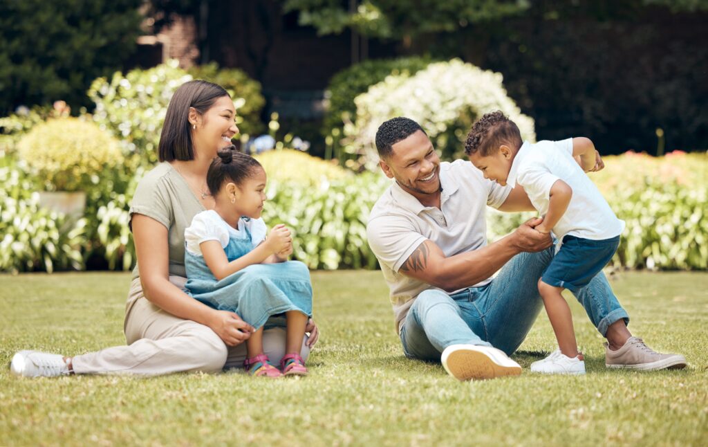 Happy family playing together on the grass, parents smiling while engaging with their children outdoors