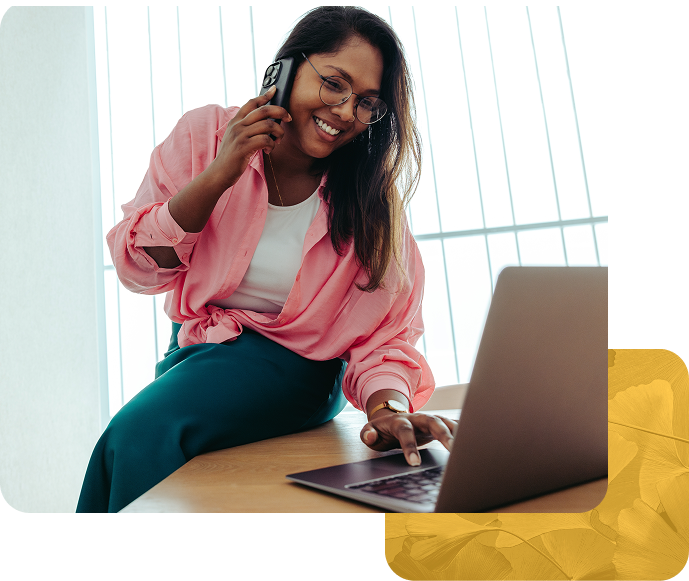 Smiling woman on phone call while working on laptop at desk